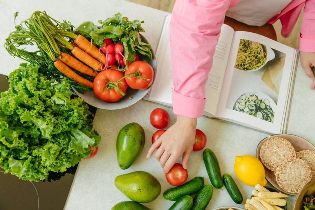 Top view of fresh vegetables and hands arranging them with a recipe book, promoting healthy eating.